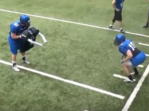 High school football players practice blocking with Colt football pad
